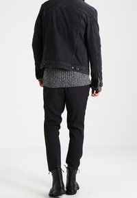 Svart denimjacka, grå stickad tröja och svarta byxor med snörning vid bensluten. Svarta ankelstövlar fulländar looken.