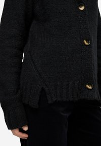 Cardigan nero lavorato a maglia con finitura testurizzata, dotato di grandi bottoni e spacchi laterali all'orlo. Maniche lunghe con polsini a coste.