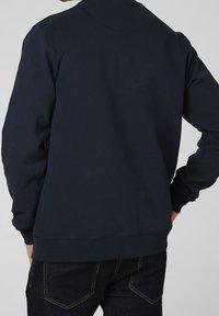 Sweat-shirt bleu marine à manches longues, col rond et poignets côtelés. Tissu en coton lisse, avec un design simple et épuré.