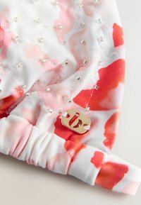 Valge lillemustriga kangast peapael, millel on pehmed roosa ja punase akvarelli-tüüpi plekid, kaunistatud läbipaistvate ja metallist helmestega ning kuldsete metallosadega.