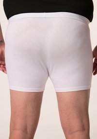 Boxer shorts bianchi in cotone con una texture morbida, cintura elastica e design minimalista. Cuciture visibili lungo i orli e i lati.