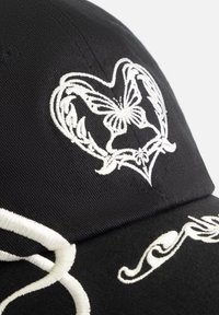 Black baseball cap featuring white embroidered designs, including a heart with a butterfly and floral accents, textured surface detailing.