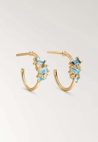 Pendientes de aro de oro con tres piedras azules rectangulares y piedras claras redondas engastadas en un diseño de garras. Acabado suave y pulido.