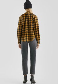 Geel en zwart geblokt overhemd met lange mouwen, rugplooien en knoopdetails; gecombineerd met grijze, gestructureerde jeans en zwarte haklaarzen.