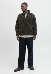 Luipaardprint fleece pullover in donkerbruin en zwart, met een halve ritssluiting, een losse pasvorm en een gestructureerde stof. Gepaard met donkere broeken.