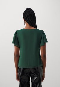 Groene blouse met korte geplooide mouwen, een soepele textuur en een ronde halslijn, gecombineerd met glanzende zwarte broeken.