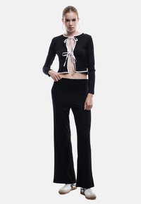 Svart ribbat crop top med vit kant och snörning, i kombination med svarta vida byxor. Modell bär vita och grå sneakers.
