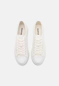 White canvas sneakers with a round toe, flat white rubber sole, and central lacing. "YOURTURN" printed on the insole. Smooth texture.