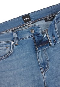 Light blue denim jeans with a slim fit, featuring a zip fly, button closure, and contrasting orange stitching. Brand label visible at the waistband.