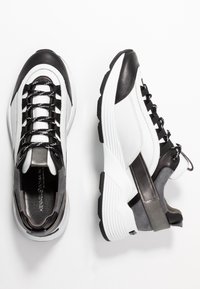 Sneaker sportive in bianco e nero realizzate con materiali in pelle, rete e camoscio, caratterizzate da una forma slanciata, suola spessa e texture a contrasto.
