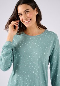 Chemise à manches longues vert menthe en tissu doux, ornée de motifs de croissants de lune et d'étoiles blancs, avec un col rond et des détails de couture.