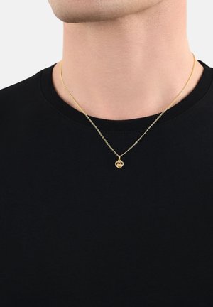 Goldene Halskette mit einem herzförmigen Anhänger, ausgestattet mit einer zarten Kette, über einem schwarzen T-Shirt getragen, das ihren Glanz und das filigrane Design zur Geltung bringt.