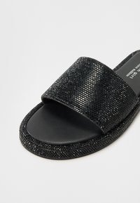 Sorte slidesandaler i svart med en bred reim prydet med rhinestones, en glatt matte fotbed, og en teksturert, solid såle.