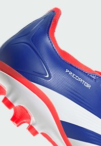 Scarpa da calcio sintetica blu con accenti rossi, tomaia testurizzata, suola bianca e l'importante marchio "PREDATOR". Presenta tacchetti visibili per la presa.