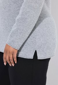 Harmaa pitkähihaine paita, joka on valmistettu pehmeästä kankaasta, jossa on sivuaukko helmassa ja tiukka malli. Yhdistetty mustiin legginsseihin.
