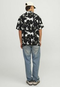 Kortærmet sort skjorte med hvidt og gyldent blomstermotiv, parret med lyseblå jeans og mørke sneakers. Kasket bæres baglæns på hovedet.