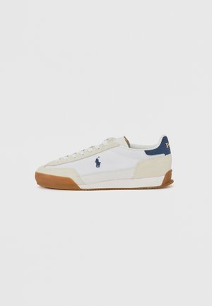 Hvite sneakers med beige semsket og mørkeblå detaljer, med gummisåle og snøring, logo på siden og hælen.