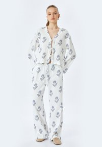 Witte, lichte tweedelige outfit met een cropped top met strik en wijde broek met een blauw bloemmotief. Soepele textuur.