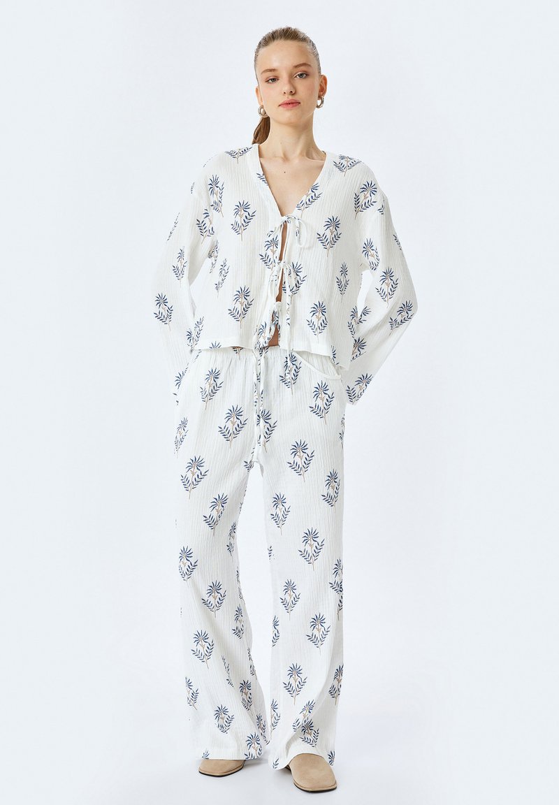 Witte, lichte tweedelige outfit met een cropped top met strik en wijde broek met een blauw bloemmotief. Soepele textuur.