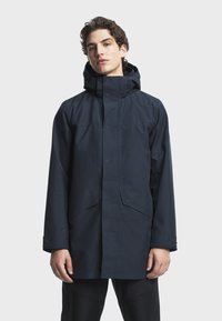 Marinblått vattentät Jacka med hög krage och justerbar huva. Har tryckknappar, sidofickor och en något lös passform. Slät textur.