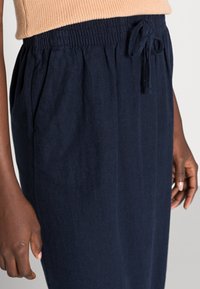 Pantalons de jogging navy à cordon de serrage, en tissu doux, avec poches latérales et taille élastique avec lien, présentant une texture lisse et un design décontracté.