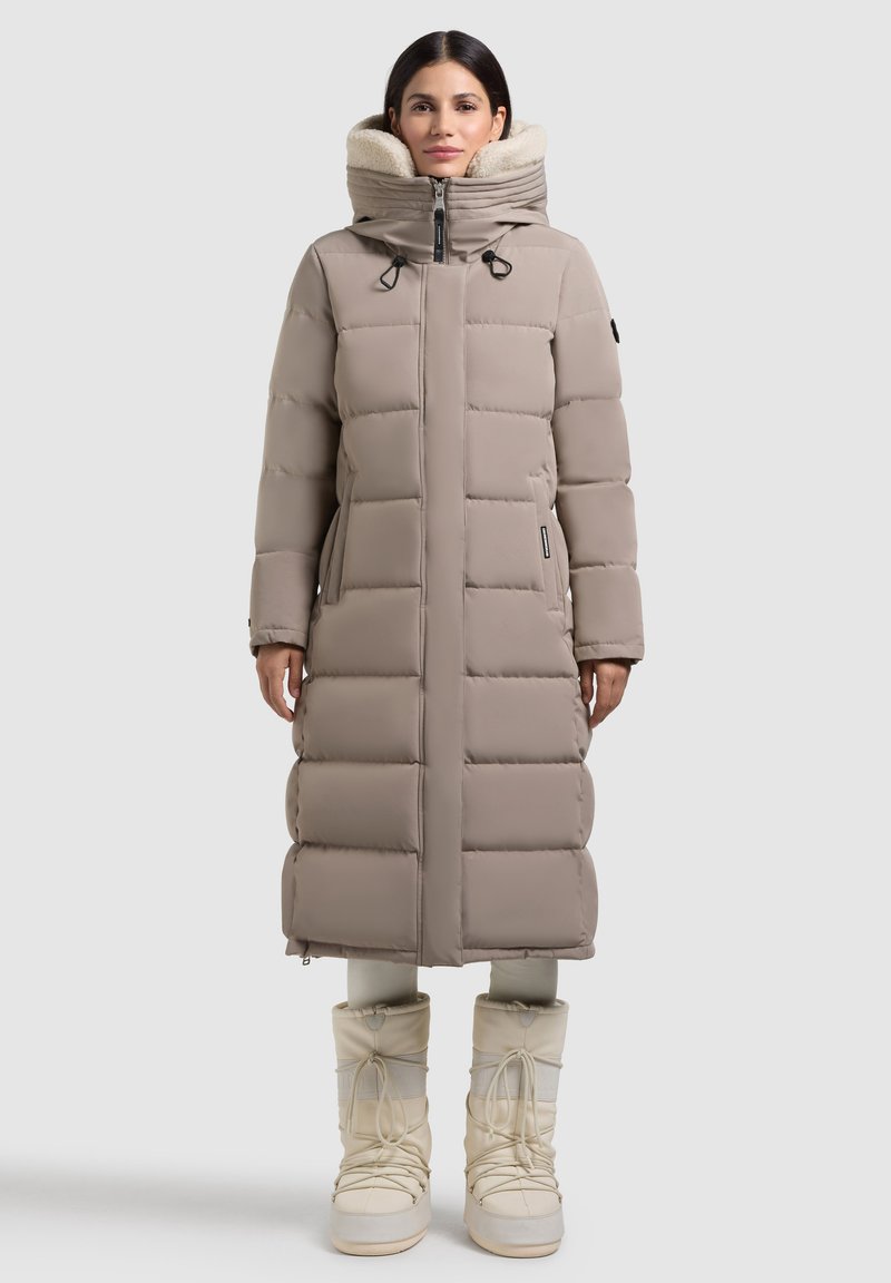 Garšs bežs pūkainais mētelis ar kvadrātveida dizainu, augstu apkakli un divām rāvējslēdzēju aizdari. Fleece oderēta kapuce un sānu kabatas. Apvienots ar baltām sniega kurpēm.