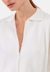 Weißer Strickcardigan mit V-Ausschnitt, einlagig und vorne mit Knöpfen. Verfügt über eine weiche Textur und klassisches Kragen-Design.