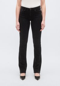 Fekete színű, karcsúsított fazonú farmernadrág, kifelé bővülő szárakkal és szórványos ezüst szegecsekkel díszítve. Puha tapintású farmeranyagból készült.