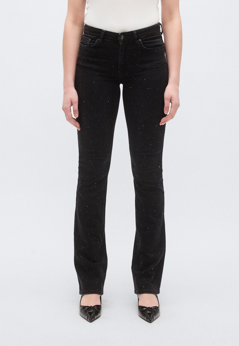 Fekete színű, karcsúsított fazonú farmernadrág, kifelé bővülő szárakkal és szórványos ezüst szegecsekkel díszítve. Puha tapintású farmeranyagból készült.