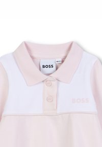 Polo en rose avec un col blanc, deux boutons roses et un subtil logo "BOSS" brodé en rose sur le devant.