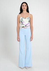 Top con motivo floreale e scollatura a cuore, abbinato a pantaloni svasati di un blu chiaro. Il materiale sembra liscio e presenta spalline regolabili.