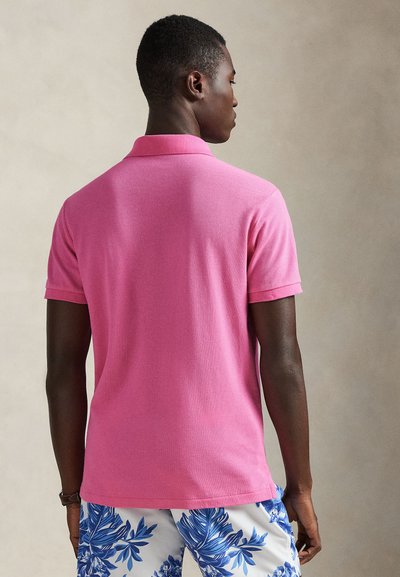 Ροζ πόλο πουκάμισο με γιακά και κοντά μανίκια, με υφή υφάσματος. Το μοντέλο φοράει μπλε και λευκά σορτς με σχέδια.