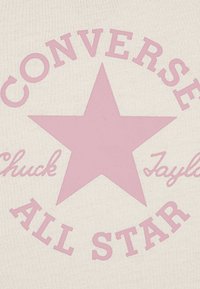 Bavlněná tkanina barvy krému s velkou růžovou hvězdou a nápisy: "CONVERSE ALL STAR" a "Chuck Taylor" růžovou barvou. Hladká textura a středový design.