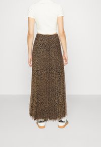 Maxi-jurk met luipaardprint in bruin en zwart, gemaakt van lichte stof met een geplooid ontwerp, gecombineerd met een wit cropped top en sneakers.