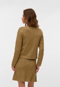 Strikket to-delt sett i en varm brun farge. Overdelen er en tettsittende genser med lange ermer; skjørtet har en A-formet design med bølget kant.