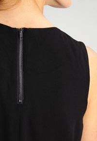 Gros plan sur le haut du dos d'une personne portant un vêtement sans manches noir avec une fermeture éclair verticale en argent.