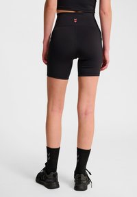 Svarta idrottsshorts med hög midja, slät yta och röda detaljer på baksidan. Bärs med svarta randiga strumpor och löparskor.