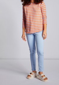 Gestreiftes langärmliges Oberteil in Orange und Hellblau, kombiniert mit hellblauen Skinny-Jeans und beigen Plateau-Sandalen.