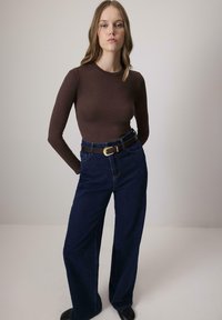 Hnedý dlhý rukáv prispôsobený top skombinovaný s vysokým pásom, širokými džínsy z tmavého denimu, s hnedým opaskom a akcentom zlatého spony.