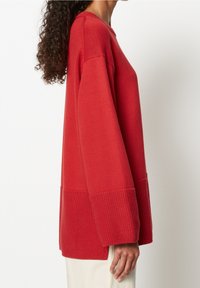 Pull tricoté rouge avec un motif texturé, doté de manches larges et d'un ourlet côtelé. Le tissu est doux et la coupe ample et décontractée.