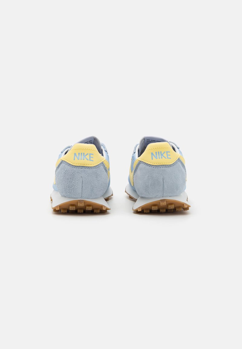 Zapatillas Nike con una parte superior de gamuza azul clara, detalles amarillos y una suela de goma beige, diseñadas para comodidad y tracción.