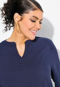 Top blu navy con scollo a V e maniche lunghe, realizzato in un tessuto liscio. Accentuato da un design semplice ed elegante e orecchini ad anello texturizzati.