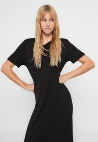 Μαύρο φόρεμα με κοντά μανίκια, άνετη εφαρμογή, απαλό ύφασμα και ελαφριά πτώση. Διαθέτει στρογγυλή λαιμόκοψη και διακριτική λεπτομέρεια στη ραφή στο πλάι.