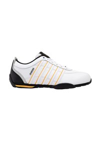 Hvid sportsko med sorte og grå accenter, der har gule striber. Glat syntetisk overdel, rund tå og struktureret gummisål.