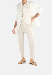 Witte blazer, lichtbeige polo en bijpassende broek. Suède loafers maken de look compleet. Soepele texturen met een minimalistisch ontwerp.
