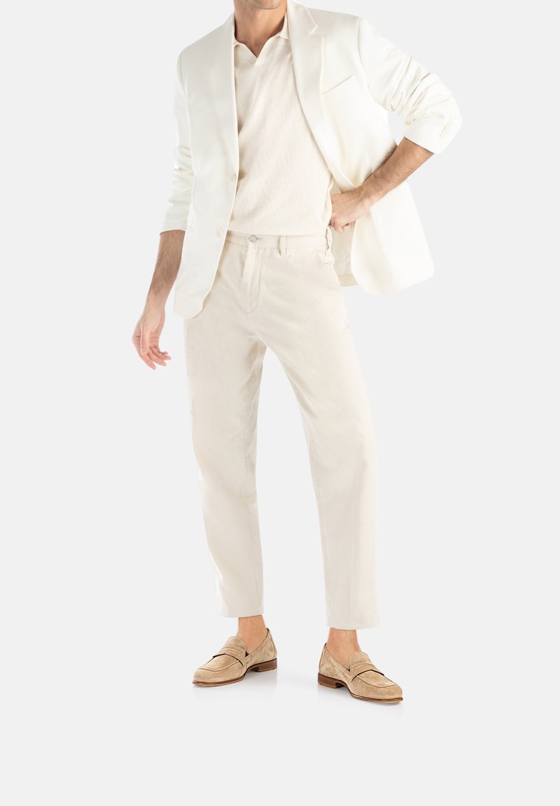 Witte blazer, lichtbeige polo en bijpassende broek. Suède loafers maken de look compleet. Soepele texturen met een minimalistisch ontwerp.