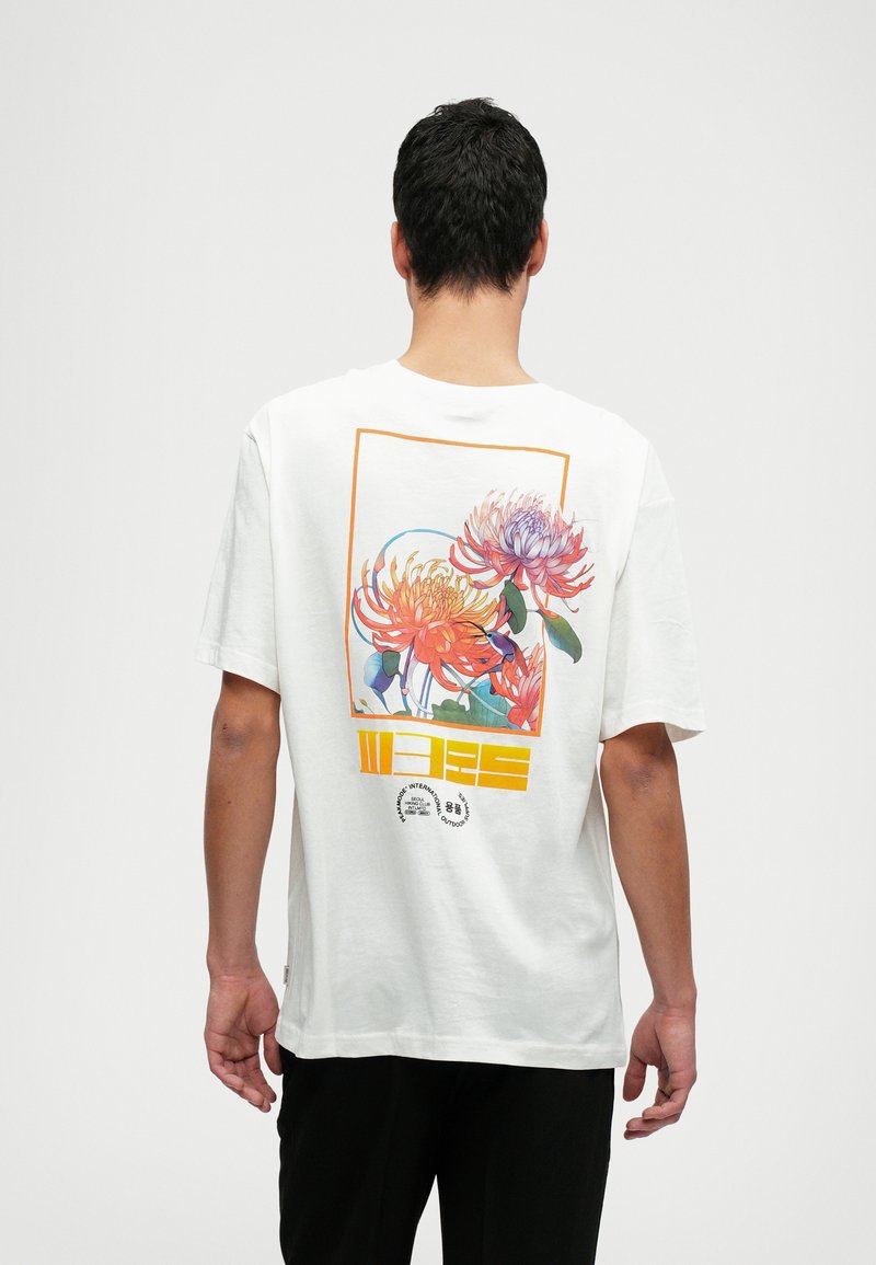 Camiseta de algodón blanca con un gráfico floral colorido en la parte posterior que presenta acentos en naranja y azul, marco rectangular y detalles del logotipo.