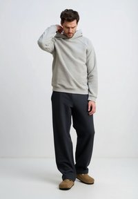 Jasnoszara bluza z kapturem z kieszenią kangurką, o luźnym kroju i ściągaczach na rękawach, zestawiona z ciemnoszarymi spodniami i brązowymi wsuwanymi butami.