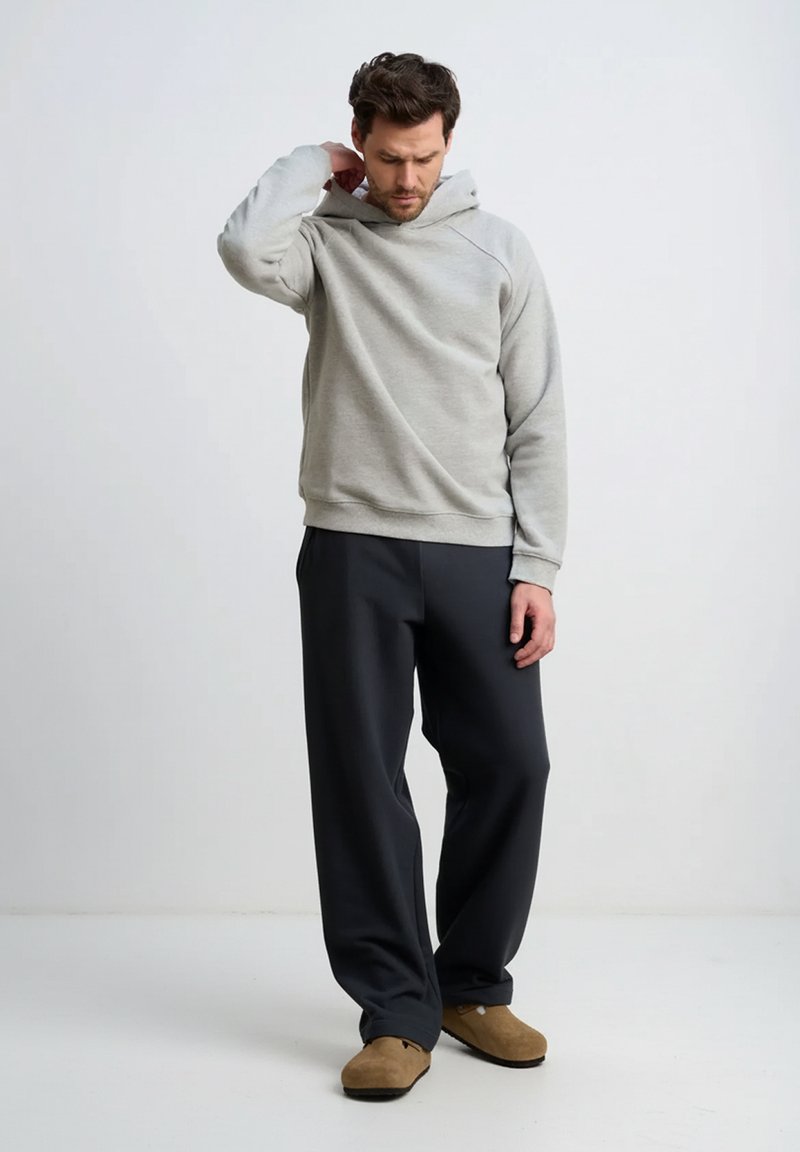 Jasnoszara bluza z kapturem z kieszenią kangurką, o luźnym kroju i ściągaczach na rękawach, zestawiona z ciemnoszarymi spodniami i brązowymi wsuwanymi butami.