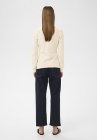 Maglione di maglia crema, jeans a gamba larga blu scuro e sandali neri bassi. Texture liscia, aderente sulle spalle, vestibilità rilassata in vita e sulle gambe.